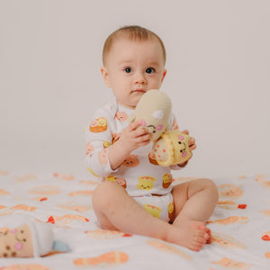 Baby sitting on a patterned blanket holding a toy, wearing a onesie with animal prints.