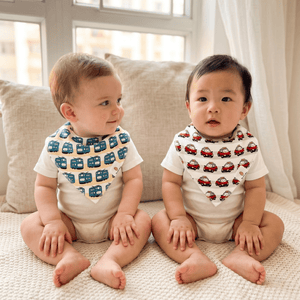 Two babies sitting on a couch wearing The Wee Bean's Transportation Bibs