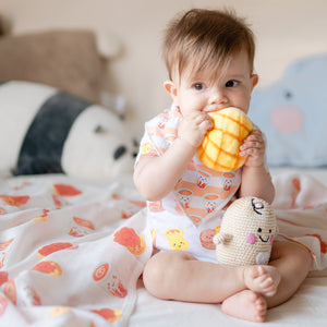 smiling baby wearing the wee bean organic cotton bib in hong kong milk tea and eating pineapple bun toy