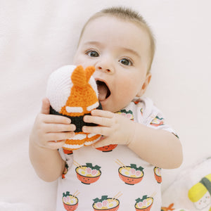 the wee bean close up of baby in organic cotton onesie in ramen noodles playing with sushi doll