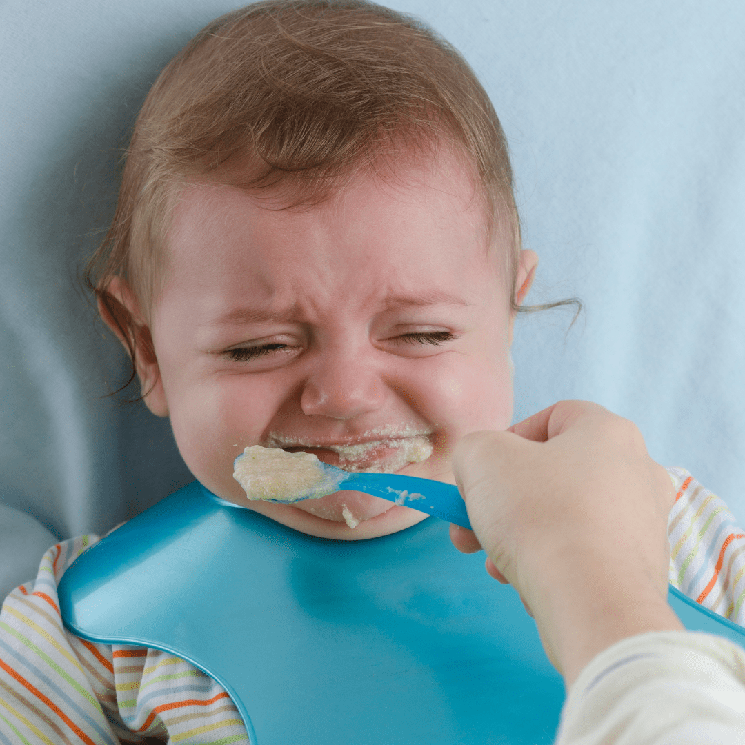 A fed baby wearing blue bib is frowning its face