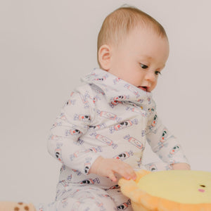 Baby wearing a patterned onesie holding a yellow plush toy against a plain background