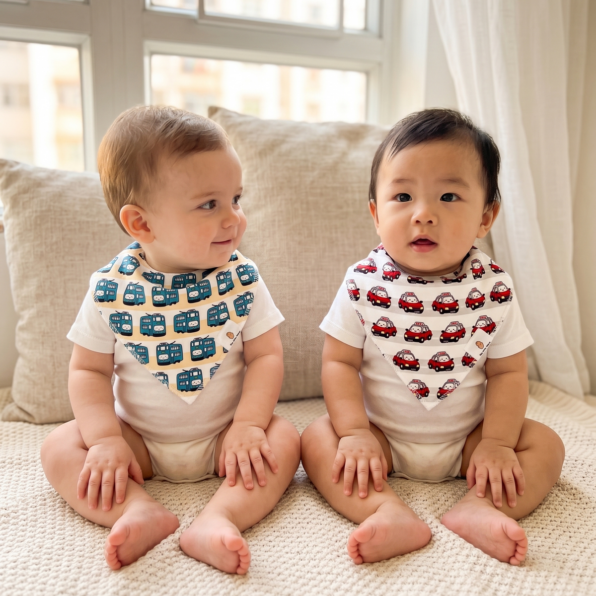 Two babies sitting on a couch wearing The Wee Bean's Transportation Bibs