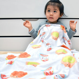 Child wrapped in a colorful blanket with cartoon designs on a white background