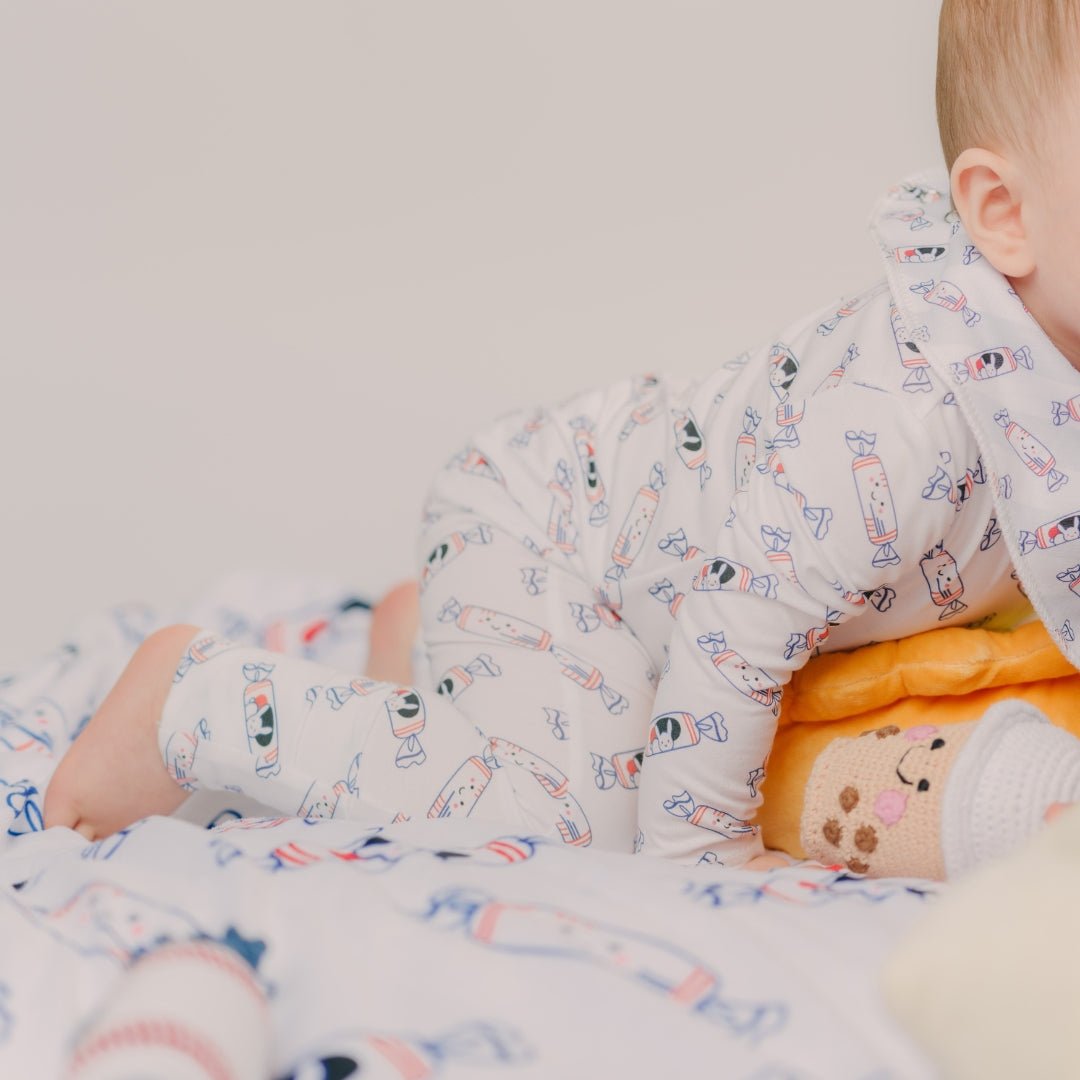 Baby in patterned pajamas lying on a soft surface with a toy.