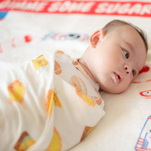Baby lying swaddled in the wee bean organic swaddle blanket with egg tart and lemon tea designs