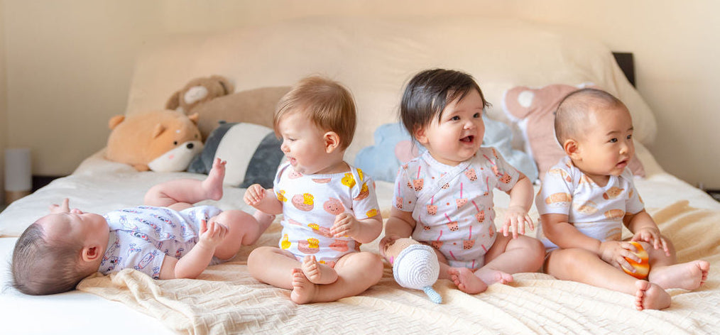 Four babies in matching organic onesies sitting on a bed.