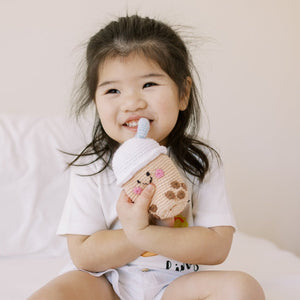 Child holding a boba crochet doll with a smile on a light background