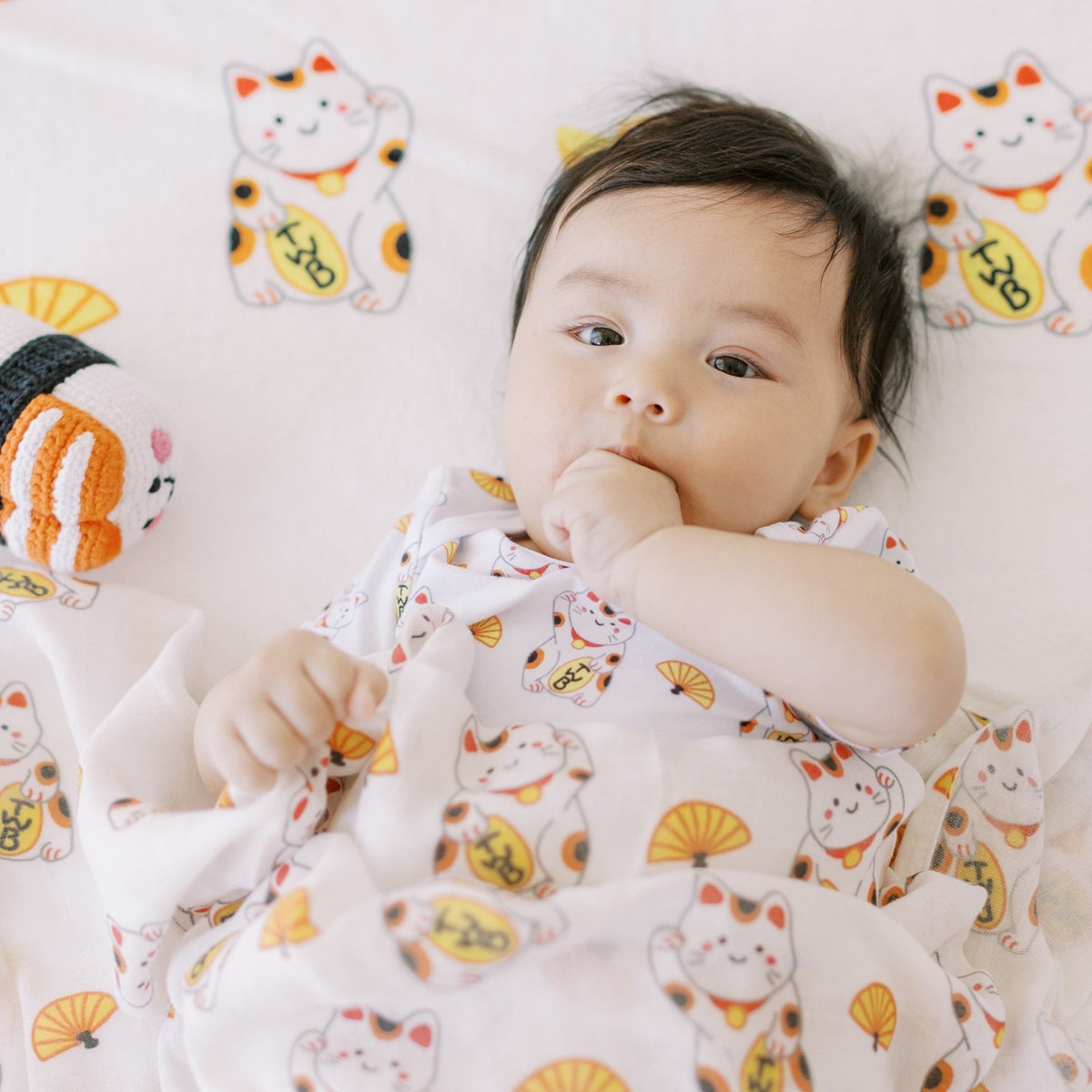 cute baby sucking thumb in lucky cat swaddle