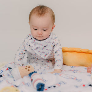 Baby in pajamas sitting on a bed with a toy, wearing a bib.