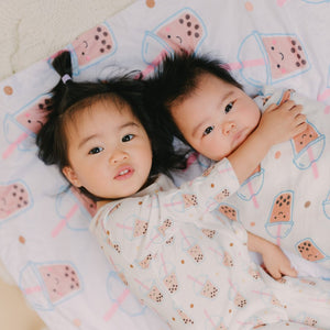 Two children lying on a blanket with a boba pattern